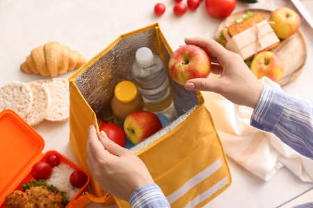 Woman packing meal into lunch box bag on light background, closeup