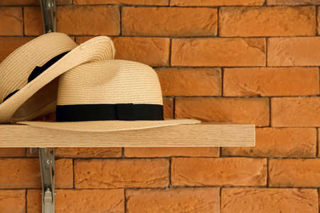 Shelf with stylish straw hats hanging on brick wallの写真素材