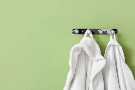 White bathrobes hanging on green wall, closeupの写真素材