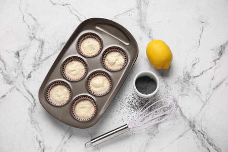 Baking tin with uncooked poppy seed muffins on light backgroundの写真素材