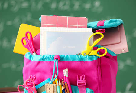 School backpack with stationery against blackboard, closeupの写真素材