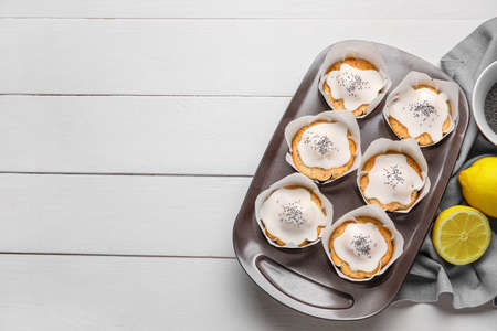Baking tin with delicious glazed poppy seed muffins on white wooden backgroundの写真素材