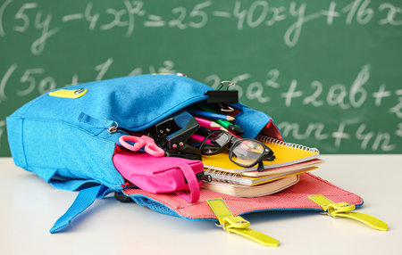 School backpack with stationery and eyeglasses on light table in classroom