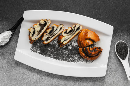 Plate with slices of tasty poppy seed bun on black and white backgroundの写真素材