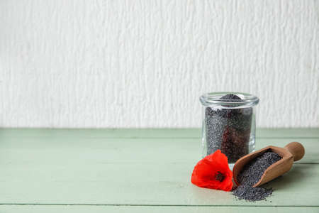 Jar and scoop with poppy seeds and flower on color wooden backgroundの写真素材