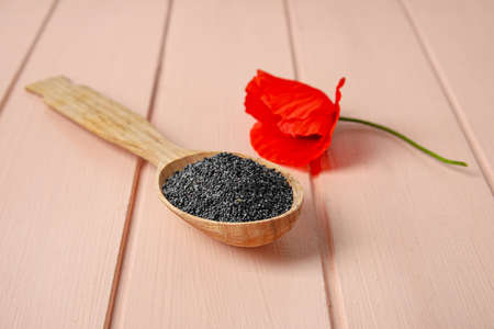 Spoon with poppy seeds and flower on color wooden backgroundの写真素材