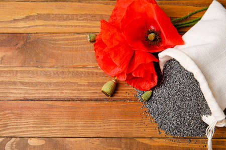 Bag with poppy seeds and flowers on wooden backgroundの写真素材