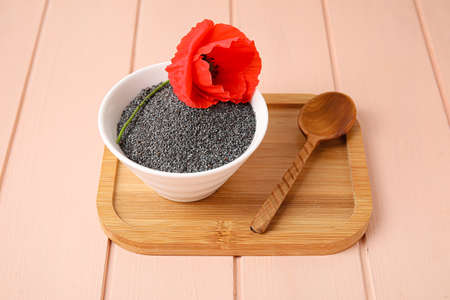 Bowl with poppy seeds and flower on color wooden backgroundの写真素材