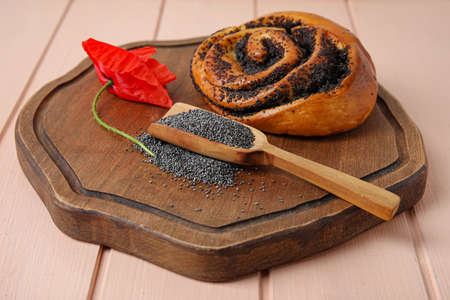 Scoop with poppy seeds, flower and tasty bun on color wooden backgroundの写真素材