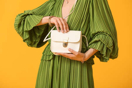Woman with trendy accessories holding handbag on color background, closeupの写真素材