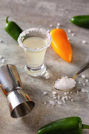 Shot of tasty tequila with chili peppers and salt on grunge background, closeup