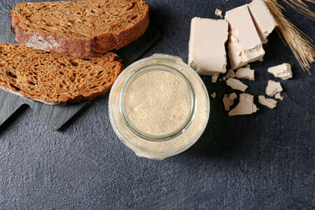 Glass jar with fresh sourdough and bread slices on black backgroundの写真素材