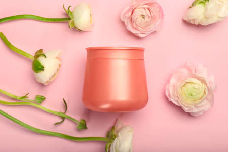 Jar of cosmetic product and beautiful ranunculus flowers on pink background