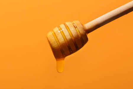 Sweet honey dripping from dipper on color backgroundの写真素材