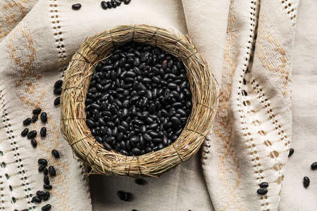 Wicker bowl with raw beans on fabric background