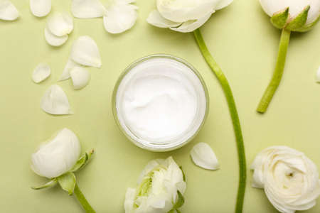 Composition with jar of cosmetic product and ranunculus flowers on green background