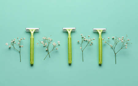Safety razors and flowers on color background