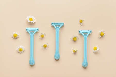 Safety razors and chamomile flowers on color background