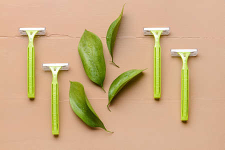 Safety razors and green leaves on color wooden backgroundの写真素材