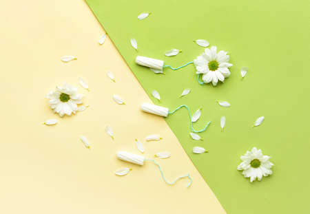 Menstrual tampons and flowers on color background