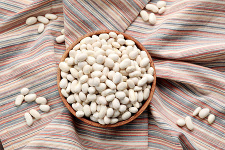 Bowl with raw beans on fabric background
