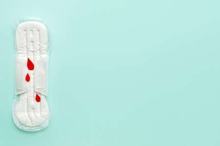 Menstrual pad and paper blood drops on blue background