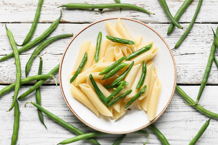 Plate of tasty pasta with green beans on light wooden background