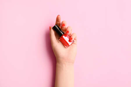 Woman with beautiful manicure holding bottle of nail polish on color backgroundの写真素材