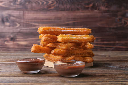 Tasty churros and melted chocolate sauce in bowls on wooden backgroundの写真素材