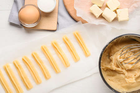 Uncooked churros and ingredients on light wooden background