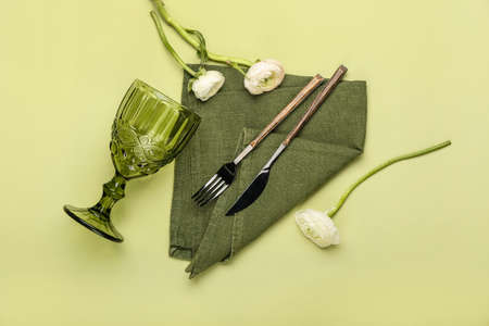 Cutlery, napkin, glass and ranunculus flowers on color backgroundの写真素材