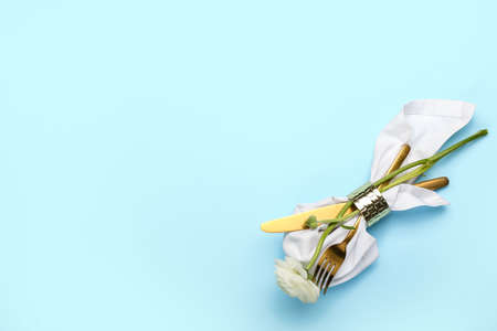 Cutlery, napkin and ranunculus flower on color background