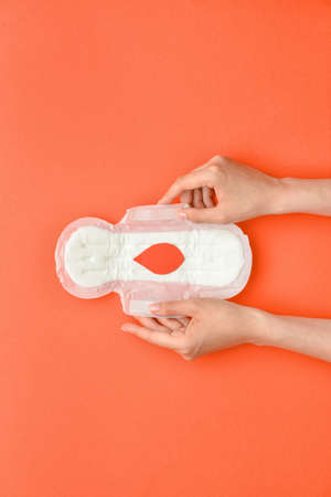 Female hand with menstrual pad and paper blood drop on red backgroundの写真素材