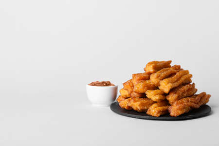 Slate plate with tasty churros and melted chocolate sauce on white background
