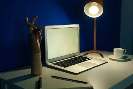 Modern workplace with open laptop and glowing lamp near blue wall in dark room