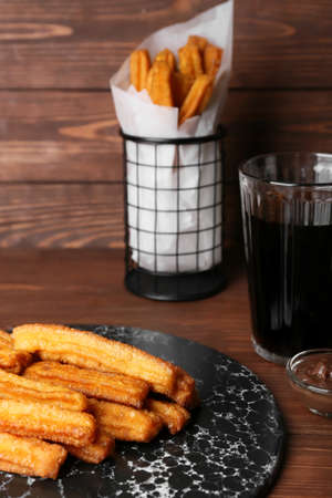 Slate plate with tasty churros, glass of cola and melted chocolate sauce on wooden backgroundの写真素材