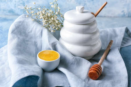 Bowl and jar of honey with flowers on color backgroundの写真素材