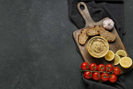 Bowl of tasty baba ghanoush, bread, lemon and tomato on black backgroundの写真素材