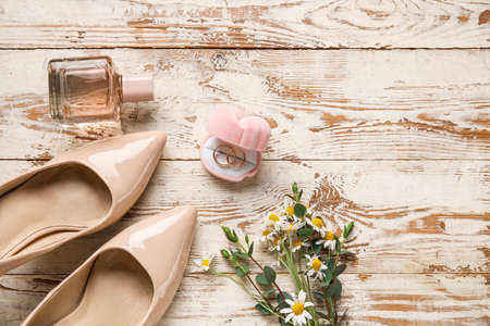 Box with wedding rings, bride shoes, perfume bottle and bouquet of flowers on light wooden backgroundの写真素材