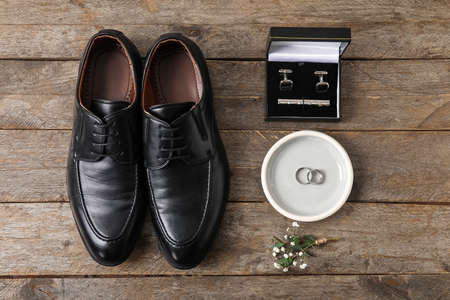 Tray with wedding rings, groom shoes and stylish male accessories on wooden background