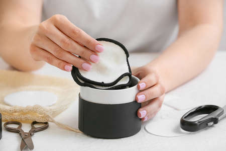 Woman putting handmade cotton pads into box at white table