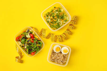 Containers with natural food and measuring tape on yellow backgroundの写真素材