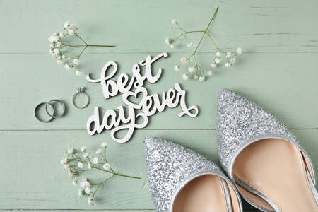 Bride shoes, wedding and engagement rings, text BEST DAY EVER on green wooden backgroundの写真素材