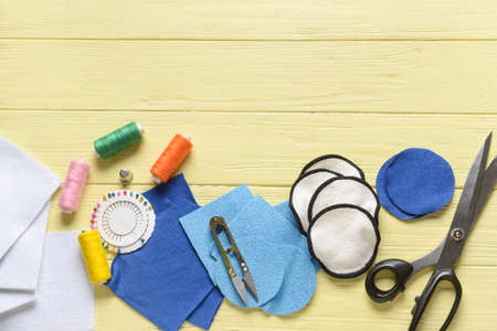 Handmade cotton pads with materials on yellow wooden background