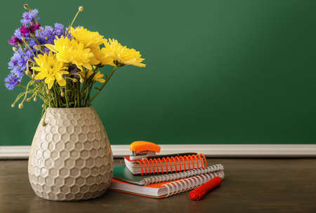 Vase with beautiful flowers and stationery on table in classroom. teacher's day celebrationの写真素材