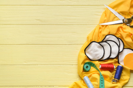Handmade cotton pads with materials on yellow wooden background