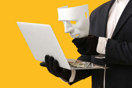 Hacker with laptop and mask on color backgroundの写真素材