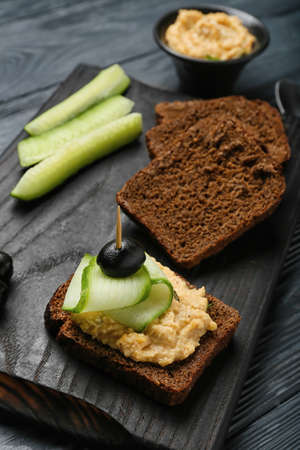 Sandwich with delicious hummus, cucumber and olive on table, closeup