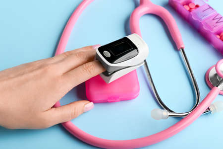 Woman with pulse oximeter and stethoscope on color background
