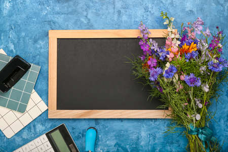 Blank chalkboard, beautiful wild flowers and stationery on color backgroundの写真素材